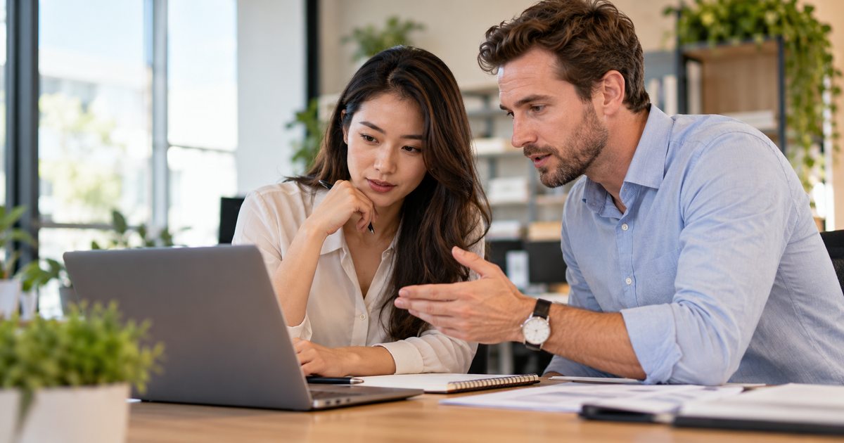 Two adult office colleagues reviewing a shared laptop in a bright modern workplace